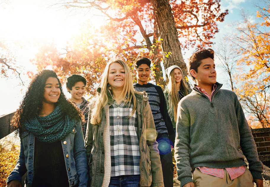 A group of teenagers walk down outdoor steps surrounded by autumn trees with sunlight shining through the leaves.