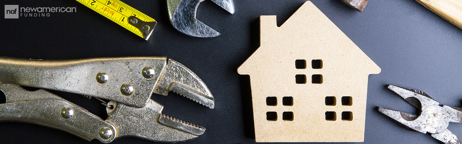 A model of a house sits on a table top surrounded by wrenches, pliers, and a tape measure