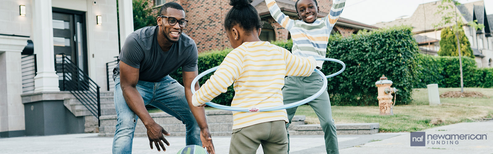 A Black man plays with his two kids in front of their home