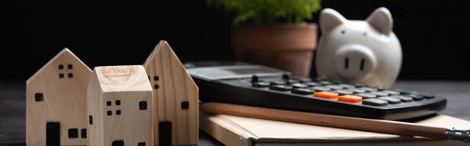 A piggy bank, calculator, and several small models of houses sit on a table