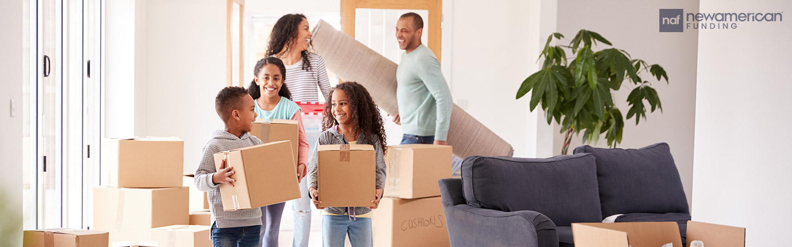 A Black man and Black woman smile at each other as they carry items into a home with their three laughing children