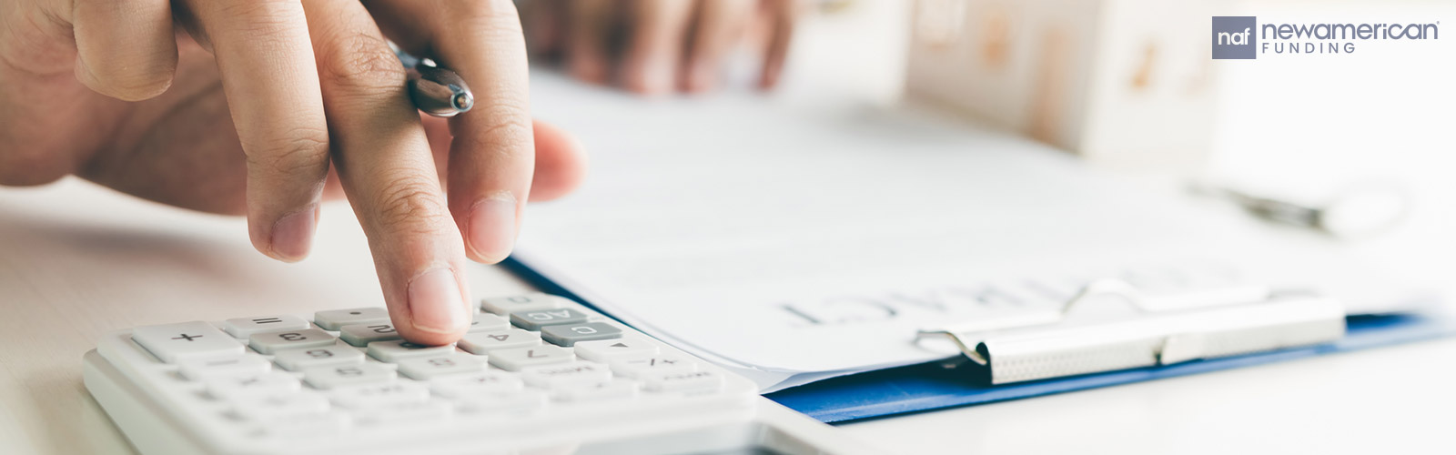A person sits at a table using a calculator and pen and paper