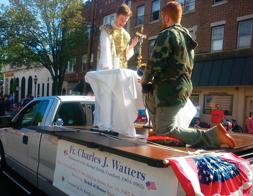 Bill (left) and Johnny Doolan, members of Cranford (N.J) Council 6226, portray Father Charles Watters with a kneeling paratrooper during the town&rsquo;s annual Memorial Day parade in 2015. Since 2013, Council 6226 has sponsored a float commemorating Father Watters, who served in Cranford before joining the Army. (Photo by John Doolan)