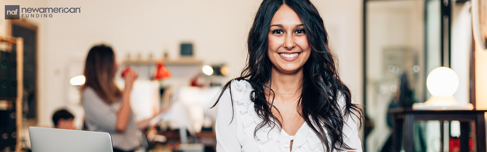 A woman sits smiling in a cafe next to a laptop