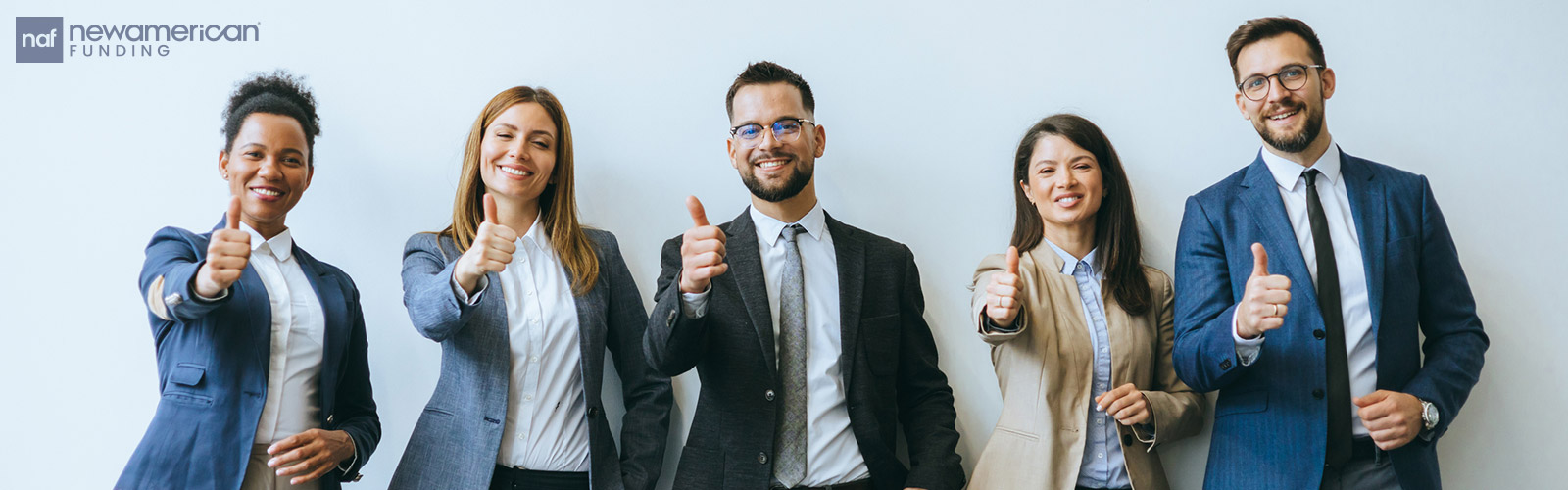 A diverse group of five people dressed in suits smile into the camera while giving a thumbs up