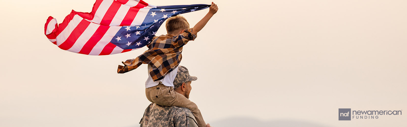 A white man in an American military uniform stands with a young boy, holding an American flag, on his shoulders