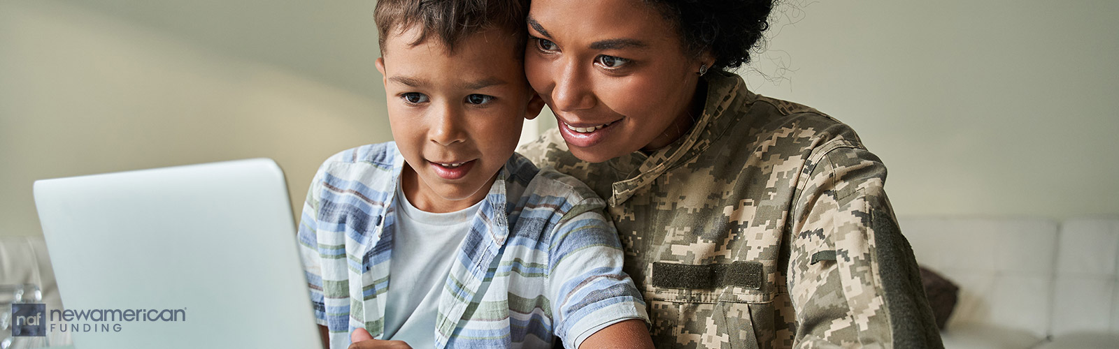 A Black woman wearing an American military uniform sits with a boy in her lap looking at a laptop