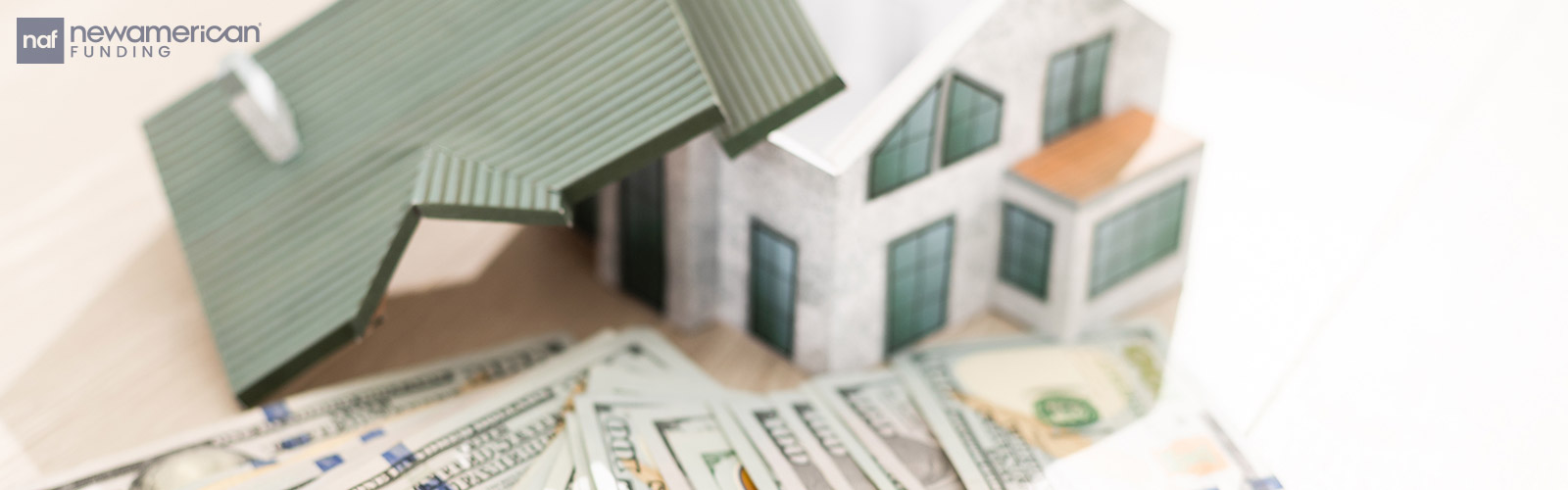 A model of a house sits on a table with a stack of hundred dollar bills