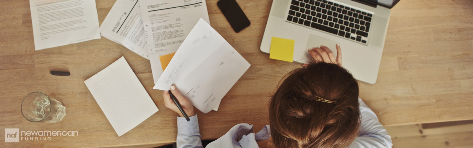 A woman sits typing at a laptop at a desk covered in papers