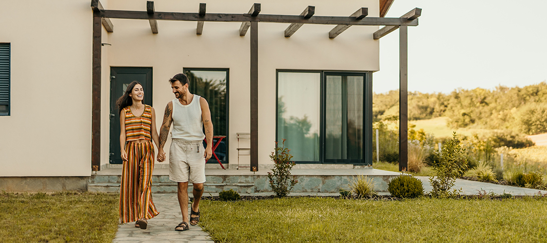 A Hispanic man and woman stand hand-in-hand in front of a nice brick home