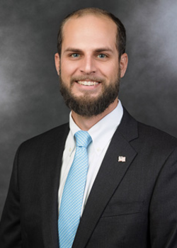 Headshot of Josh Paton, who smiles while wearing a black suit and a light blue tie