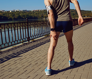 Moški se drži na nogo, ker si je pri teku nategnil mišico.