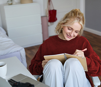 Študentka sedi v spalnici in v zvezek zapisuje svoje SMART cilje, vezane na življenjski projekt.