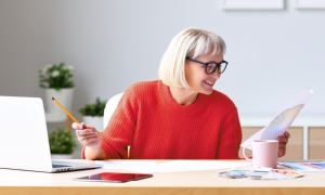 Ženska sedi v svoji domači pisarni in samozavestno pregleduje svoj mesečni proračun, saj ve, kaj je varčevanje in za kaj varčuje.