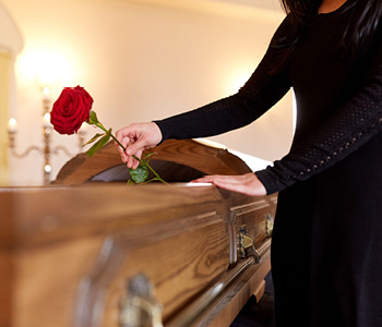 Ženska z vrtnico v roki na pogrebu stoji ob krsti svojca