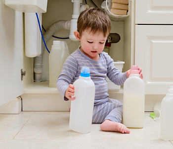 Malček se igra v kopalnici s čistili, ki jih je našel v omari - simbolna slika za zaščito otrok doma