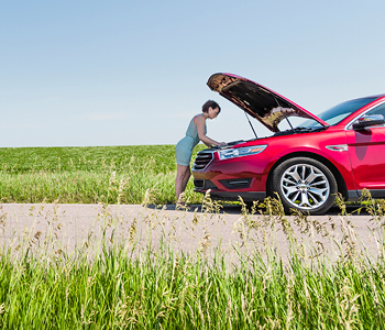 Ženska gleda pod pokrov vozila v motor, ker se ji je avto pokvaril sredi ceste