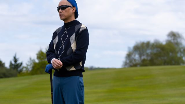 Ken Leung as Eric Tao stands on a golf course holding a club, wearing sunglasses and a patterned sweater.