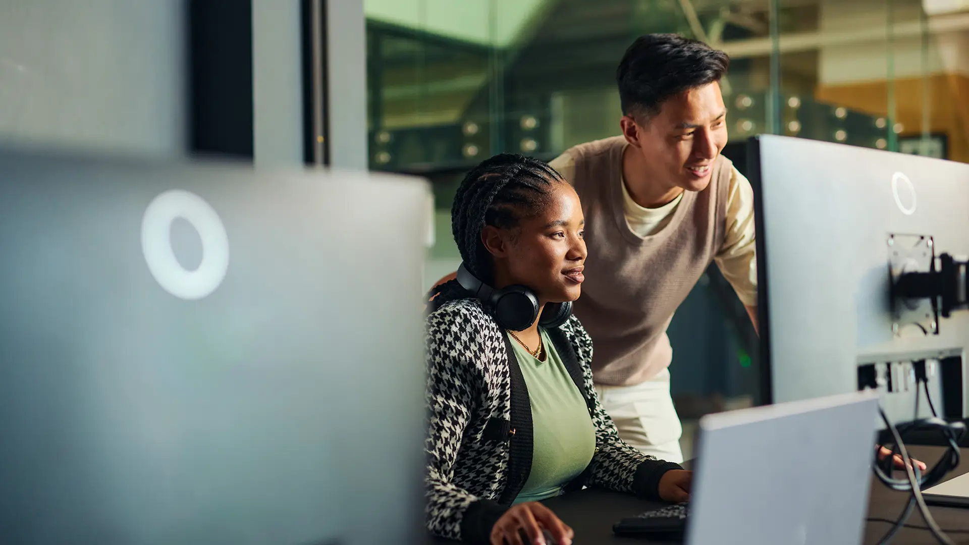 Two coworkers working together at desktop computers in an office.