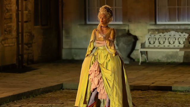 Marisa Abela as Yasmin Kara-Hanani stands outdoors in an elaborate yellow period gown, arms crossed