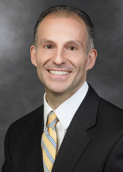 Michael Prinzivalli, who smiles while wearing a black suit and a yellow and blue striped tie