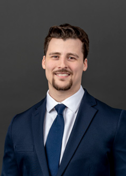 Headshot of Morgan Dudley, who smiles while wearing a dark blue suit and a blue tie