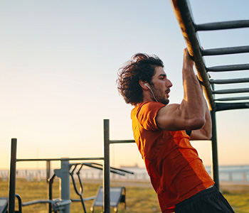 Mlad tekač izvaja vaje za moč na zunanjih vadbenih napravah.