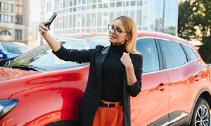 Mlada ženska ponosno pozira za sebek ob vzorno bočno parkiranem vozilu.