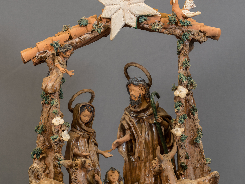 Photo of a clay Nativity scene from Portugal featuring the Holy Family within a stable. An ox, donkey, and rooster look upon them. 