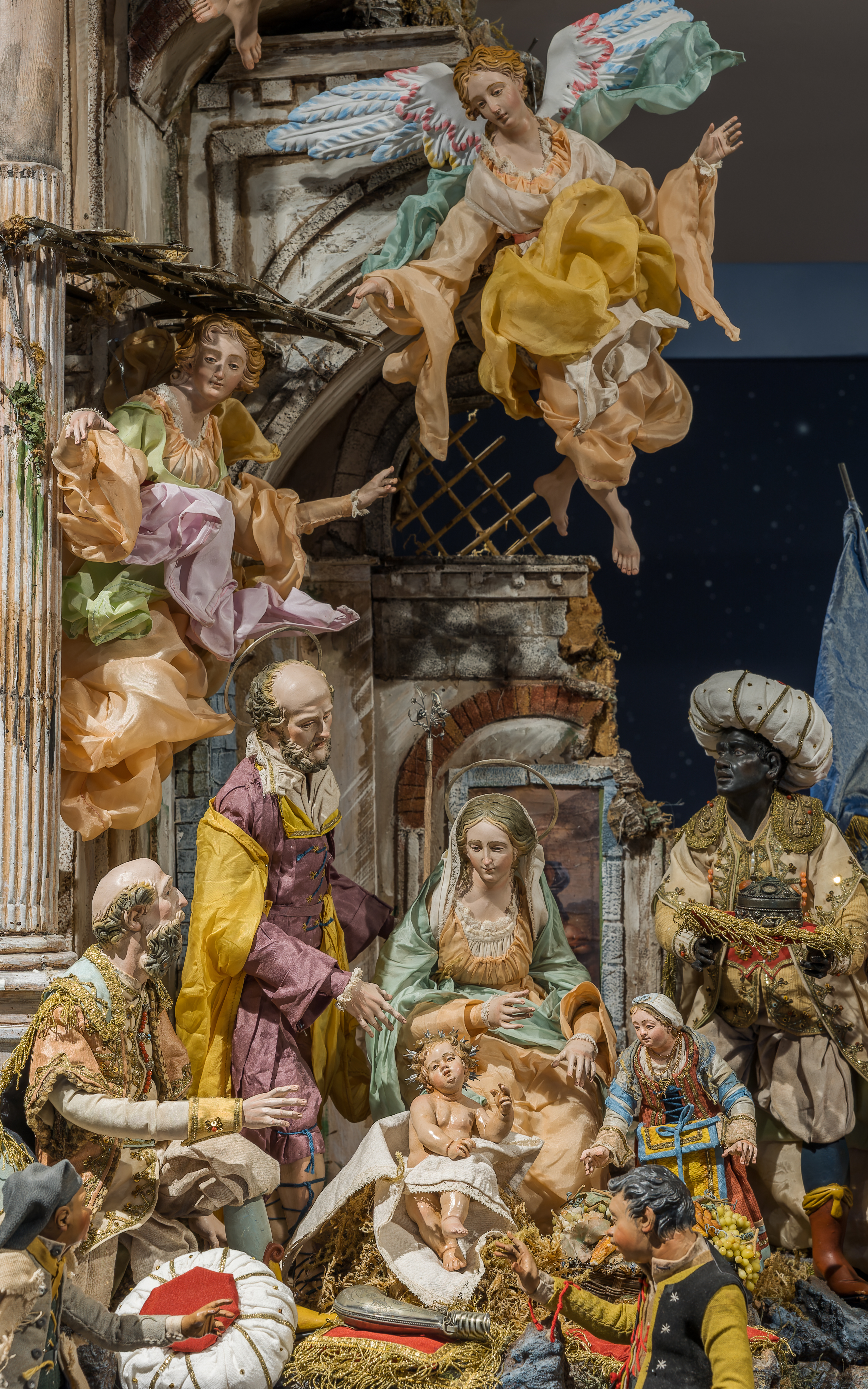 Detail photo of a Neapolitan crèche by Cantone and Costabile featuring the Holy Family among Roman ruins with two Magi, two shepherds, and three townspeople looking on. 