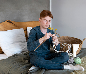 Najstnik sedi na postelji v svoji sobi in plete.