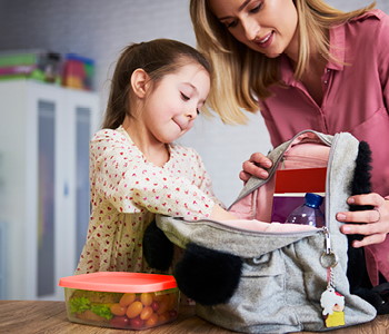 Mama hčerki pomaga v šolski nahrbtnik pospraviti šolske potrebščine.