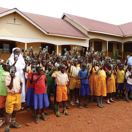 Students at the Marengoni Primary School in Uganda hold up prayer cards featuring the prayer for the canonization of Father McGivney.