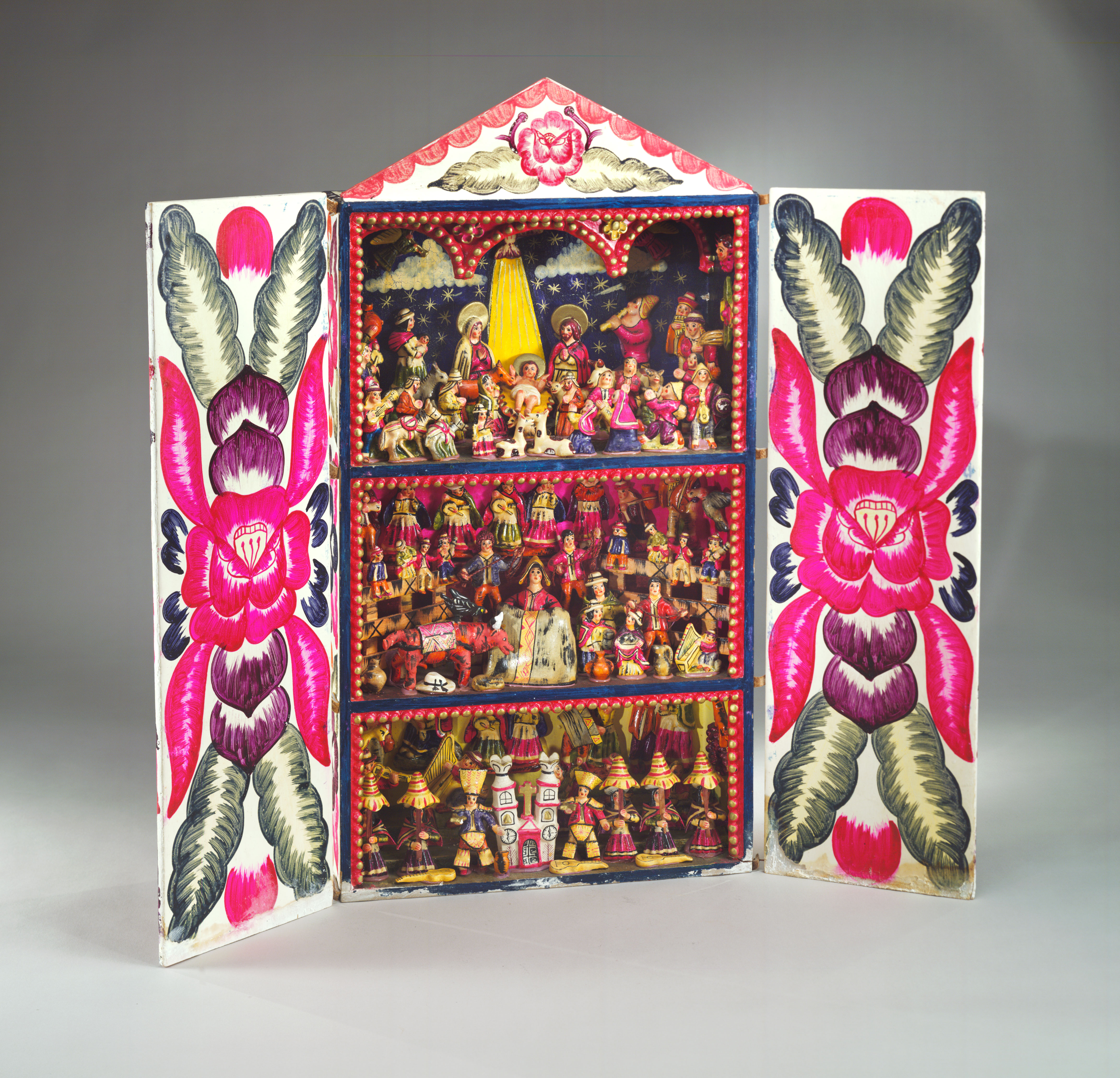 Nativity on the top shelf of 3 shelves in a potable box with doors painted with floral patterns. The other 2 shelves show scenes of Peruvian culture.