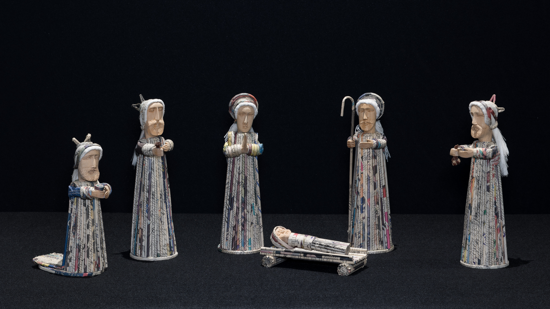 Photo of a Nativity scene made of wood and rolled newspaper featuring figures of the Holy Family and 3 Magi.