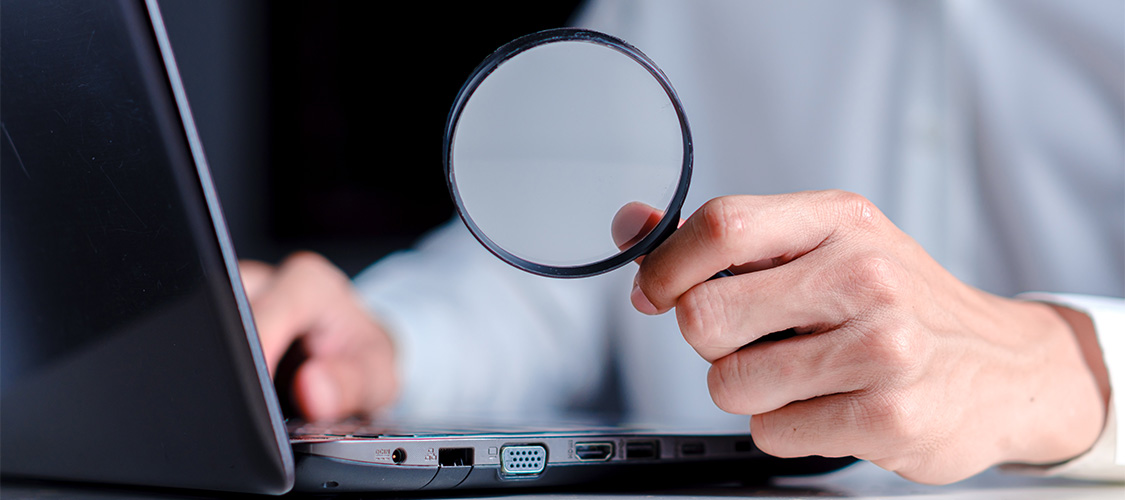 Someone holding a magnifying glass while looking at a laptop
