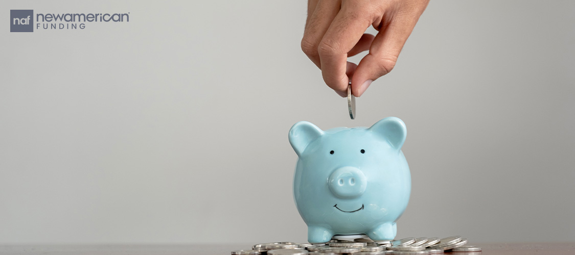 A hand dropping a coin into a blue piggy bank