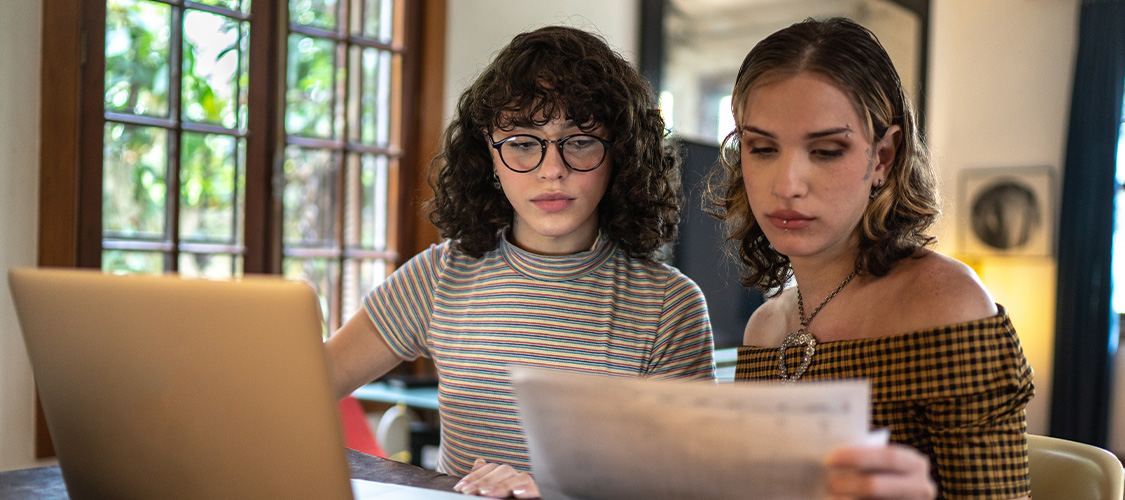 Two young people looking at paperwork and a laptop