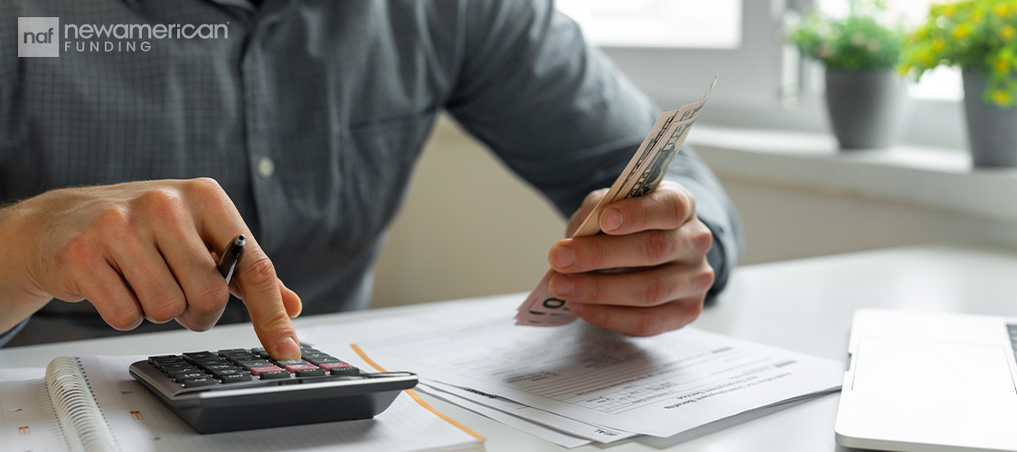 Someone holding cash in one hand and working on a calculator in the other.