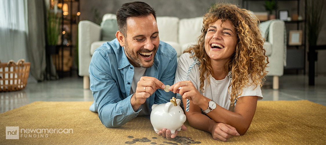 A couple laughing as they put money in a piggy bank.