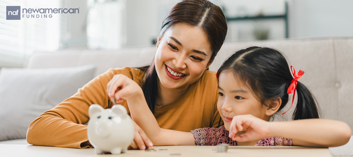 A little girl putting a coin in a piggy bank next to her smiling mother.