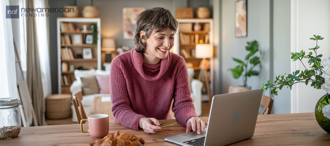 A smiling woman sitting at a desk in front of an open laptop.
