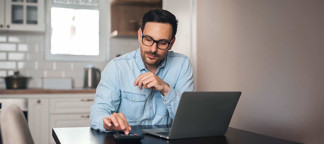 A man on a calculator looking at a laptop.