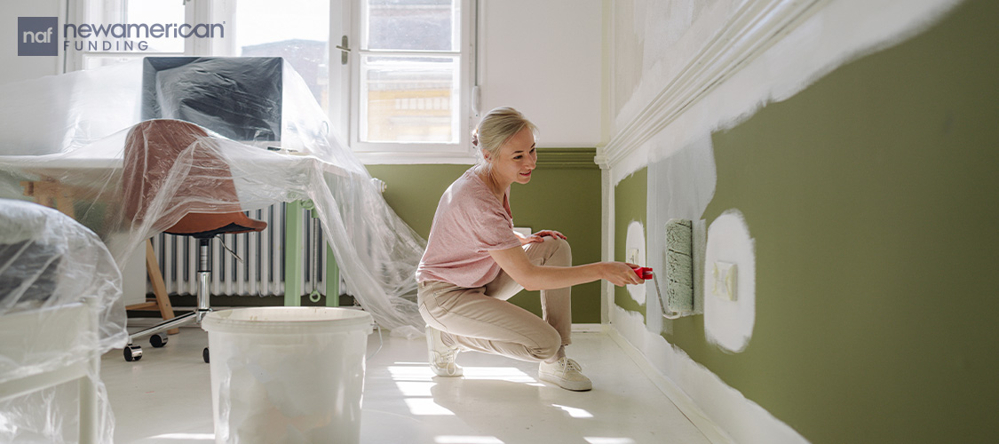 A woman painting a wall green.