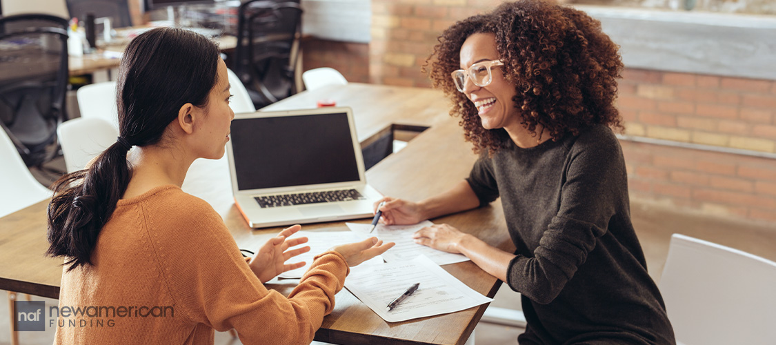 Two women talking while sitting at opposite ends of a desk.