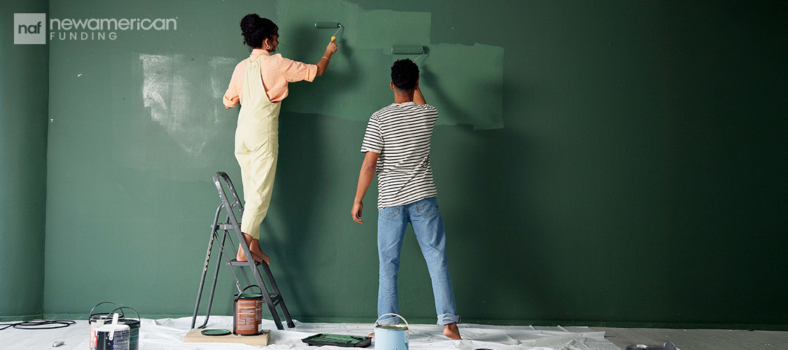 A couple painting a wall green.