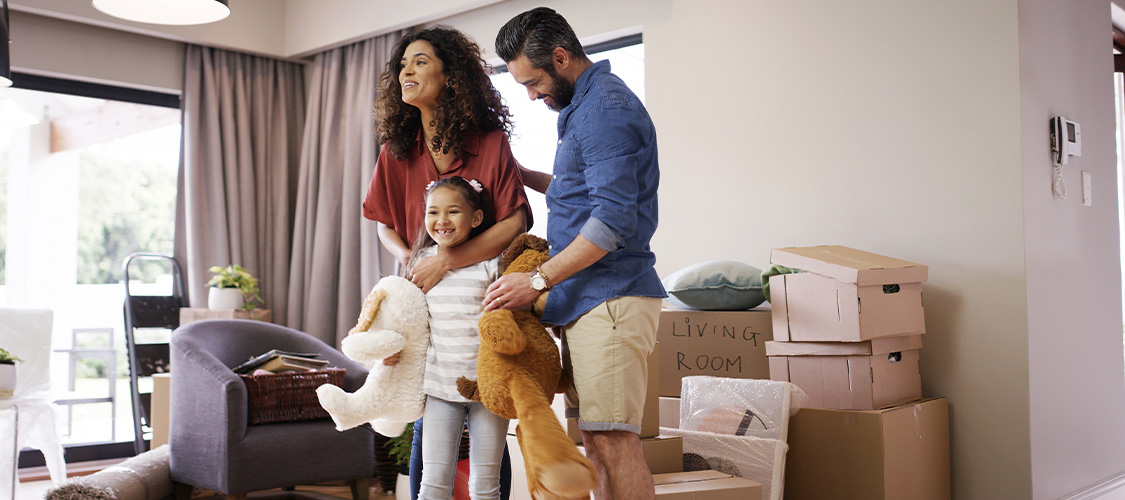 A family and a little girl holding teddy bears in a room filled with boxes.