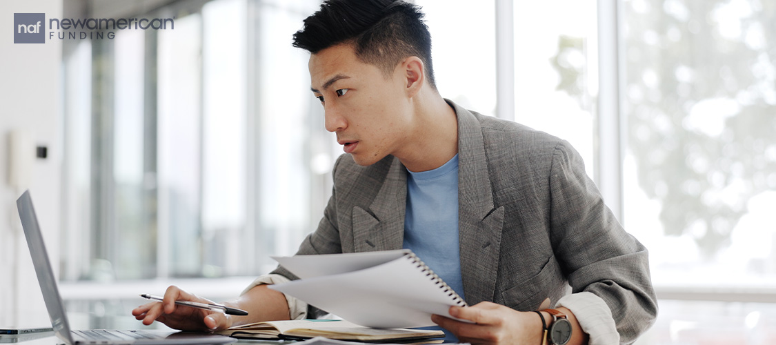 A man looking at a laptop and paperwork,