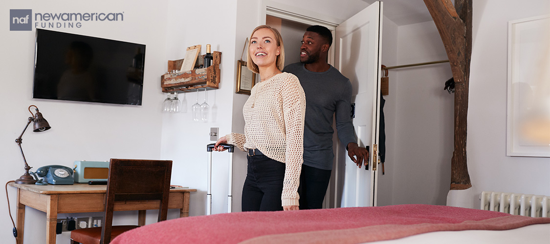 A couple walking into a room with suitcases.