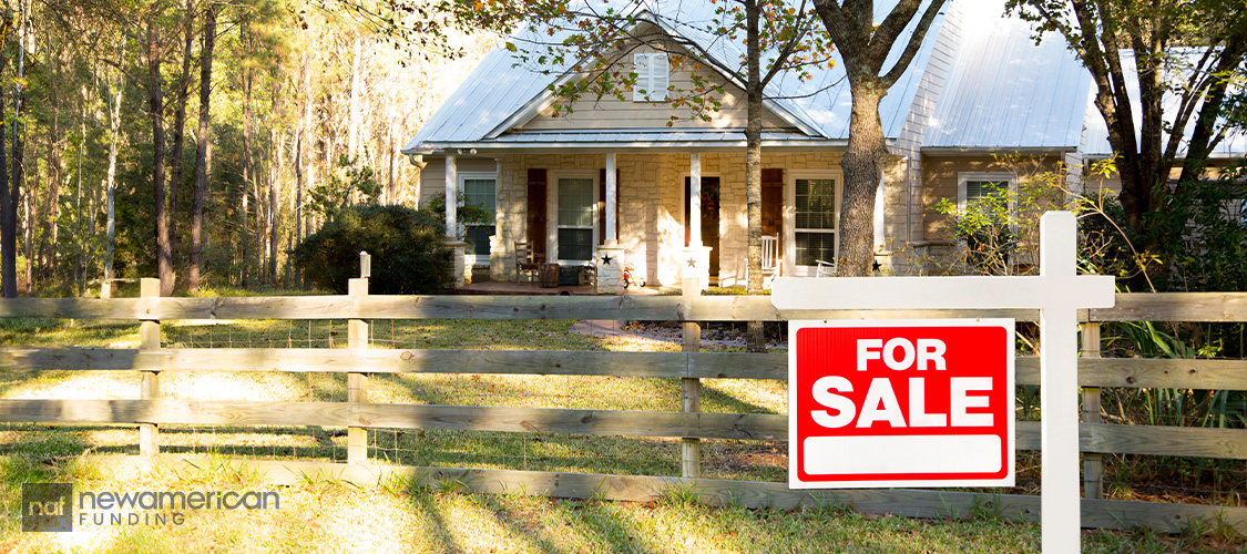 A for-sale sign in front of a home in a rural area.